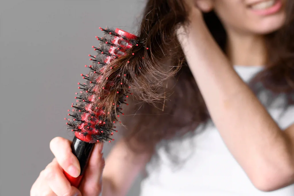 A woman brushes her hair using a red and black hairbrush, showcasing her grooming routine and personal care.