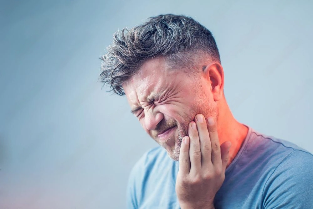 A man grimaces in pain, holding his jaw, indicating he is suffering from a toothache.